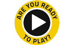 A circular icon with a yellow border and black centre, featuring a white play button in the middle and the text 'ARE YOU READY TO PLAY?' written around the edge in bold yellow and black font.
