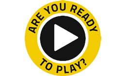 A circular icon with a yellow border and black centre, featuring a white play button in the middle and the text 'ARE YOU READY TO PLAY?' written around the edge in bold yellow and black font.