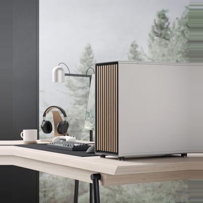 Chillblast Hygge computer from the Hej collection in White, featuring a sleek minimalist design with wooden slat detailing, set on a stylish wooden desk with a modern keyboard, headphones, and a serene forest view through the window.