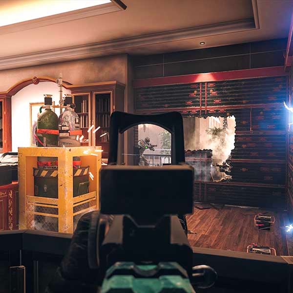 First-person view in Rainbow Six Siege showing a player aiming through a holographic sight at a destructible wall with a hole breached, exposing an enemy in a reinforced room.