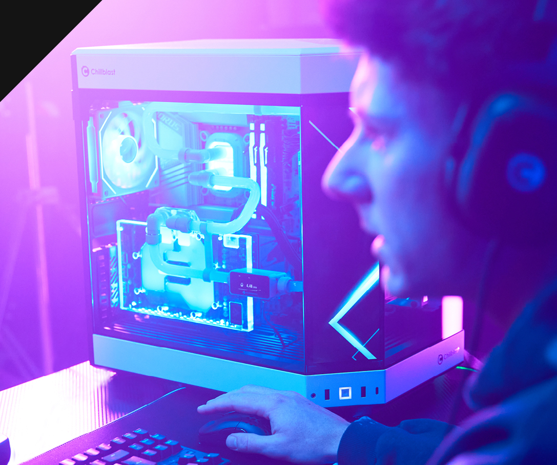 Chillblast Verge PC showcased in a vibrant gaming setup, featuring glowing blue liquid cooling and RGB lighting inside a sleek, white chassis, with a gamer wearing a headset and actively using the system in a purple-lit environment.