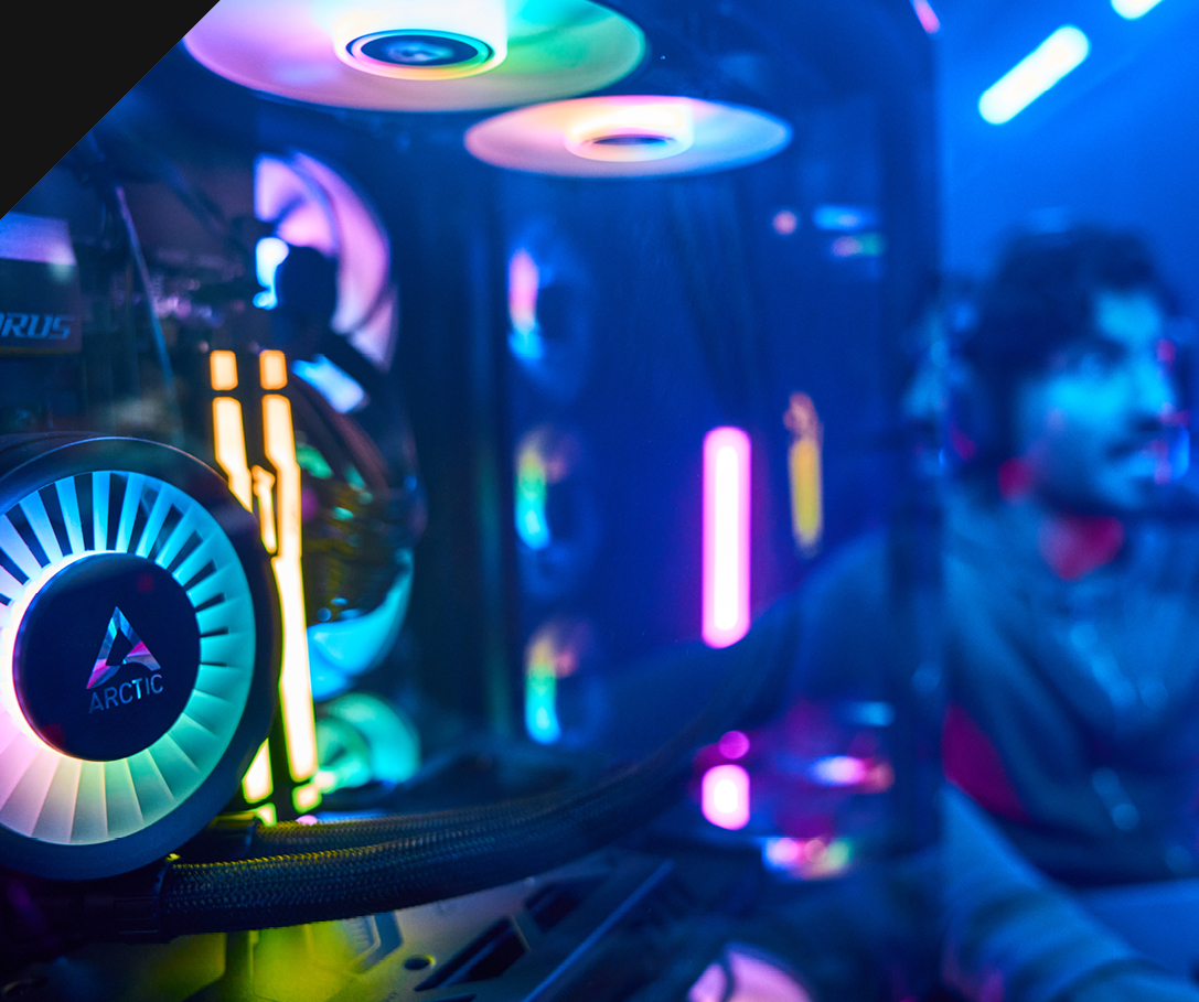 Close-up of the Chillblast Vertex PC showcasing the Arctic liquid cooling system and vibrant RGB lighting, with colorful fans and illuminated internal components, set in a dynamic gaming environment with a blurred gamer in the background.