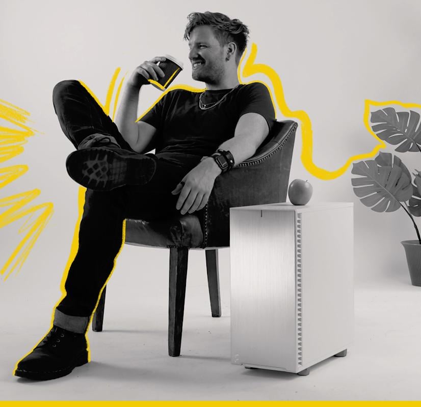 A Chillblast Spark Video Ultra Workstation computer placed next to a person relaxing in a chair, holding a coffee cup, with a minimalistic setup featuring a potted plant and an apple on the PC, accented with bold yellow graphic highlights representing creativity and comfort.
