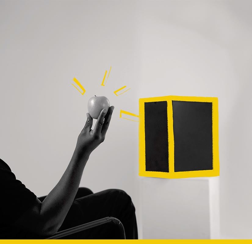 A Chillblast Spark Video Ultra Workstation computer with a sleek black design, accented with bold yellow highlights, placed on a stand while a person holds an apple in a contemplative pose, symbolizing creativity and inspiration.